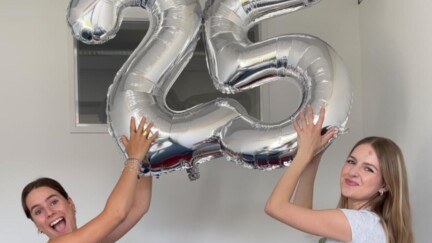 Zwei Frauen halten jeweils eine silberne Ballonzahl nach oben und lächeln. Die Ballons ergeben eine 25.