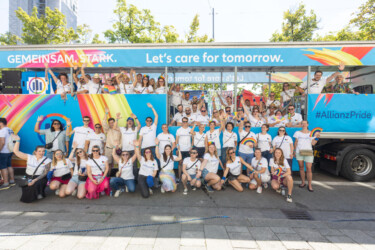 Mitarbeiter der Allianz, die in bunten Farben vor einem Truck stehen, der mit "Gemeinsam stark. Let's care for tomorrow. #AllianzPride" beschriftet ist.