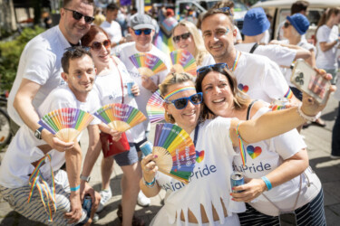 Mitarbeiter der Allianz mit "#AllianzPride"-T-Shirts und Regenbogen-Fächern in den Händen.