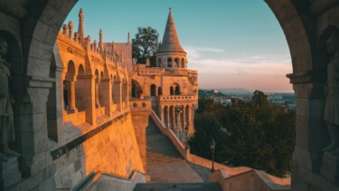 Die Fischerbastei in Budapest leuchtet rötlich im Sonnenuntergang. Im Hintergrund sieht man die Ausläufer der Stadt