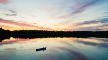 Eine Person rudert in einem Kanu über einen See in Lappland, der den Sonnenuntergang spiegelt.