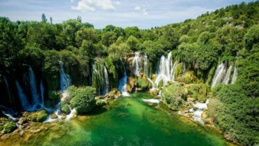 An den Kravica Wasserfällen speisen viele kleine Wasserfälle einen türkis-grünen See, der von Wald umgeben ist.
