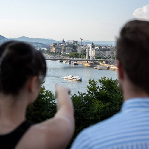 Zwei Menschen stehen auf Hügel und zeigen auf Budapest.