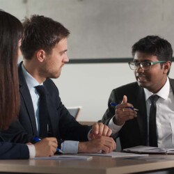 Studierende im Anzug unterhalten sich am Tisch.