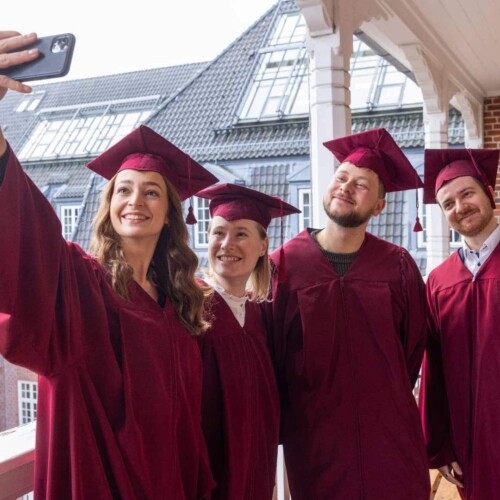 Studierende in roten Gewändern machen ein Selfie.
