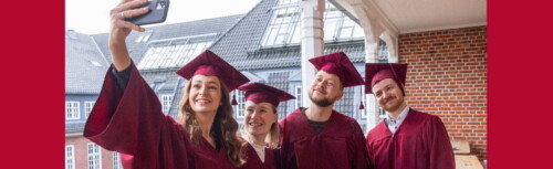 Studierende in roten Gewändern machen ein Selfie.