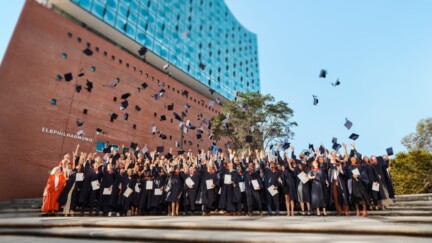 Studierende werfen Absolventenhüte in die Luft und stehen unter der Elbphilharmonie.