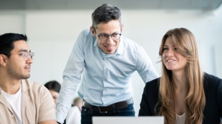 Vier Studierende sitzen gemeinsam im Seminar und tauschen sich mit einem Dozenten aus.