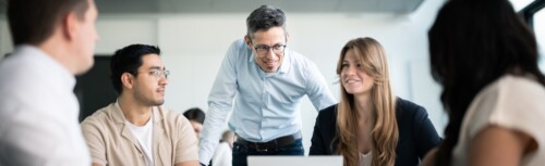 Vier Studierende sitzen gemeinsam im Seminar und tauschen sich mit einem Dozenten aus.