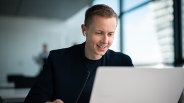 Ein Student mir AirPods sitzt im Seminarraum und schaut auf seinen Laptop.