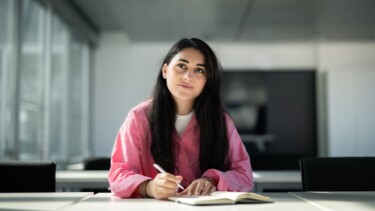 Eine Studentin sitzt im Seminarraum und macht sich Notizen.