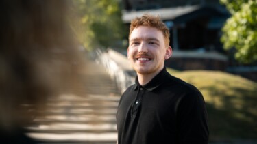 Ein Student steht auf dem Campus und lächelt.