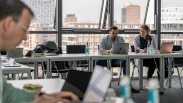 Leute sitzen an Tischen und arbeiten am Laptop.