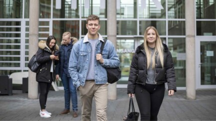 Studierende kommen aus einem Gebäude und laufen auf die Kamera zu.