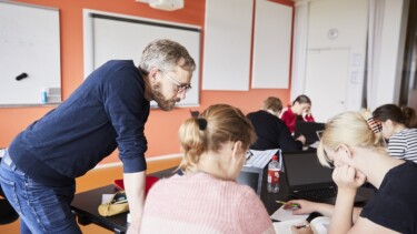 Lehrer schaut bei Schülern auf Aufgaben.