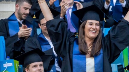 Studierende im Talar feiern ihren Abschluss mit Applaus und Jubel.