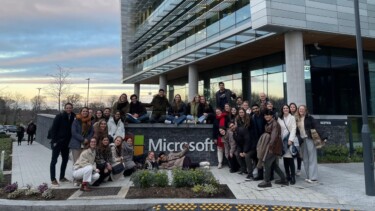 Große Gruppe Studierender posiert lachend vor dem Microsoft-Gebäude für ein Gruppenfoto.