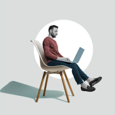 Ein Mann sitzt mit Laptop auf dem Schoß auf einem leicht zu großen Stuhl. Die Beine baumeln in der Luft.