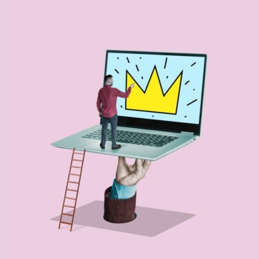 Hand hält Laptop. Auf dem Laptop steht ein Mann und schaut sie die darauf abgebildete Krone an.