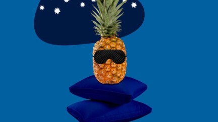 Eine Ananas sitz auf zwei Kissen und hat eine Schlafmaske auf