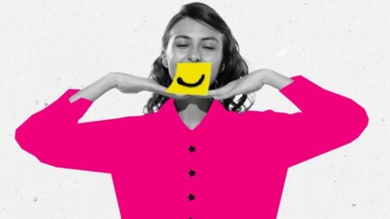 Eine Frau hat ein Stück Papier vor ihrem Mund auf dem ein lachendes Smiley abgebildet ist