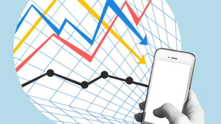 Hand hält Handy. Im Hintergrund ist eine Statistik zu sehen, die von Finanzen handelt.