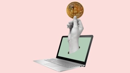 Hand schaut aus einem Laptop raus und hält einen Bitcoin.