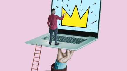 Hand hält Laptop. Auf dem Laptop steht ein Mann und schaut sie die darauf abgebildete Krone an.
