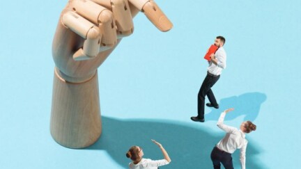 Großer Zeigefinder einer Hand zeigt auf Geschäftsmann, zwei Geschäftsfrauen im Schatten der Hand halten schützend ihre Arme vor sich