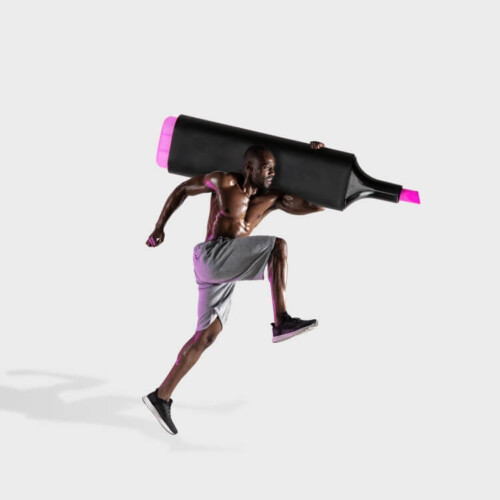 Ein Mann in sportlicher Kleidung sprintet. Er trägt einen überdimensionierten Textmarker auf der Schulter.