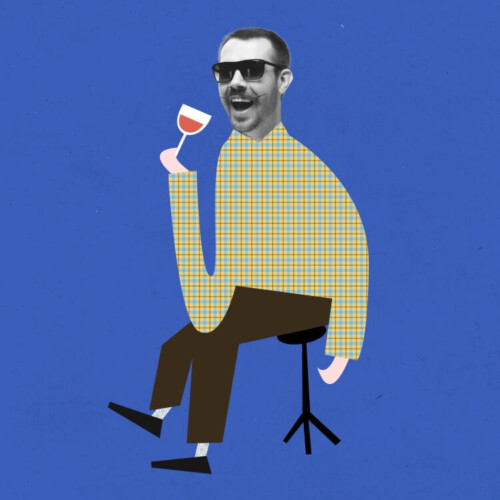 Lächelnder Mann mit Sonnenbrille sitzt auf einem Hocker und trinkt aus einem Weinglas.