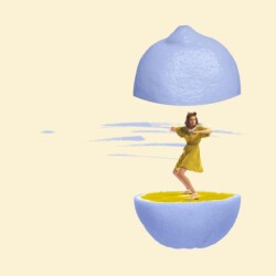Eine Frau tanzt zwischen den angeschnittenen Hälften einer Zitrone. Die Schale der Zitrone ist lila gefärbt.