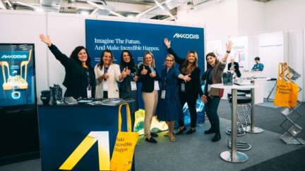 Mitarbeitende von Akkodis stehen auf einer Messe an einem Stand und winken in die Kamera.