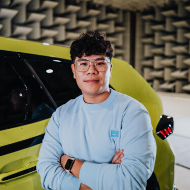 Junger Mitarbeiter steht vor einem gelben SUV