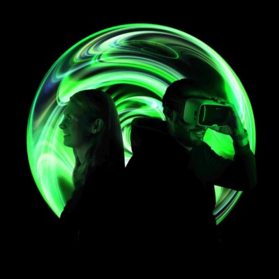 Frau uns Mann stehen Rücken an Rücken. Der Mann trägt eine VR-Brille.