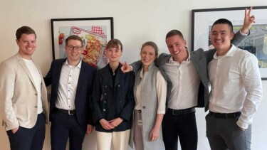 Sechs Personen stehen gemeinsam vor einer Wand mit Bildern.
