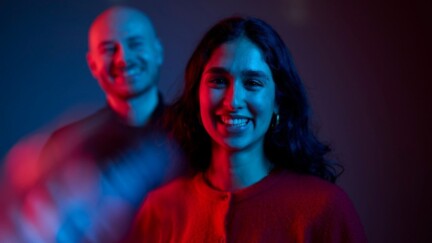 Lächelnde Frau im Vordergrund. Hinter ihr steht ein Kollege