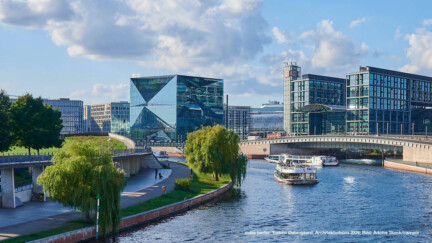 Quelle: cube berlin: Torben Østergaard, Architekturbüro 3XN; Bild: Adobe Stock/campix. Blick auf den Cube in Berlin mit Schiff auf dem Fluss davor
