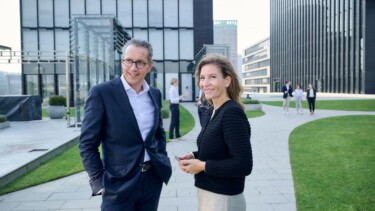 Zwei Mitarbeiter:innen und Horn & Company stehen im Innenhof eines Bürokomplexes.