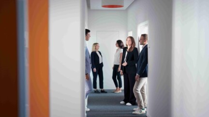 Personen stehen in einem Bürogang und unterhalten sich miteinander.