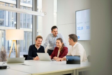 Drei Männer und eine Frau sitzen zusammen an einem Besprechungstisch
