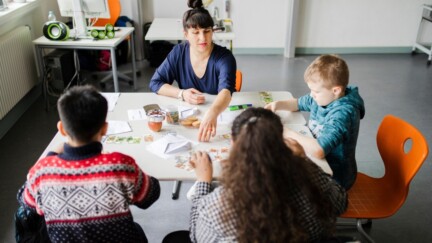 Eine Gruppe von Schüler:innen sitzt am Tisch und wird von einem Fellow begleitet.