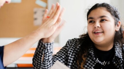 Ein Mädchen lächelt in die Kamera und klatscht eine Hand ab.