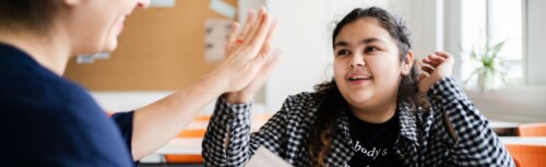 Ein Mädchen lächelt in die Kamera und klatscht eine Hand ab.