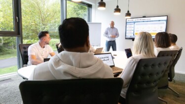 Ein Team sitzt an einem Konferenztisch und schauen auf einen Bildschirm, auf dem Statistiken zu sehen sind.