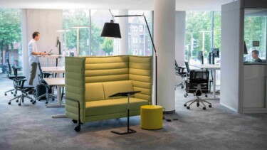Offenes Büro mit grüner Couch und Steharbeitsplätzen.