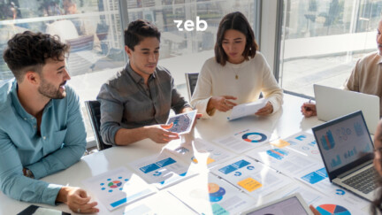 oben in der Mitte das zeb Logo in weiß, im Hintergrund eine Szene eines Teams am Tisch sitzend, das verschiedene Grafiken bespricht