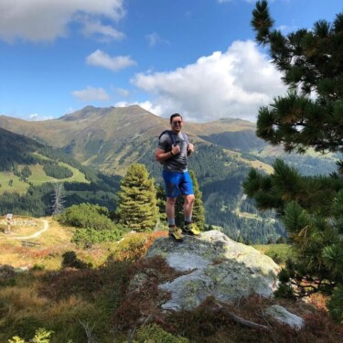 Mann, der in einer Berglandschaft steht, über ihm blauer Himmel und weiße Wolken