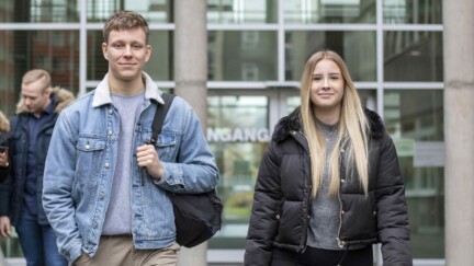 Studierende kommen aus einem Gebäude und laufen auf die Kamera zu.