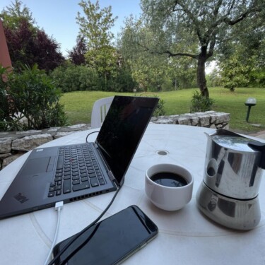 Laptop, Smartphone, Kaffeekanne und -tasse auf einem Tisch im Garten